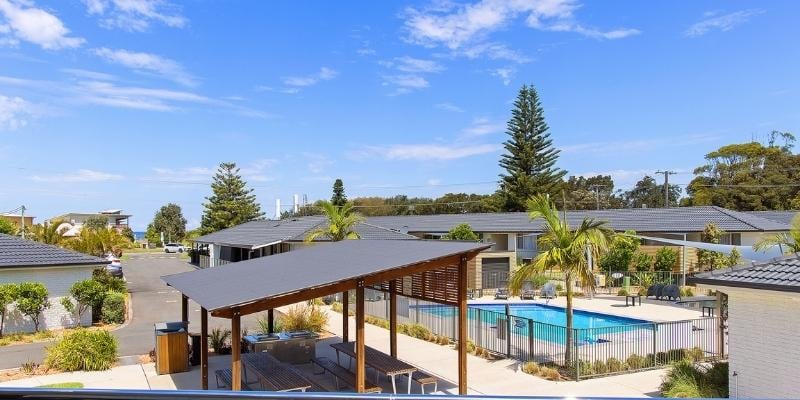 Story-based intervention - My Holiday at Seaside Holiday Resort in Fingal Bay  -  Wheelchair accessible BBQ area and picnic seating next to pool area with view of the ocean in the distance
