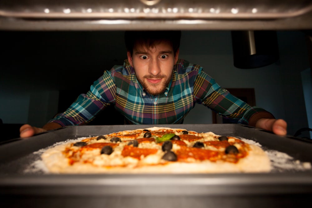 Image of man taking pizza from oven
